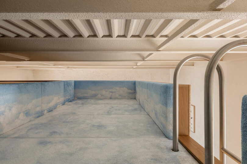 Loft bed with blue cloud-patterned padding and walls, metal ladder, and textured ceiling overhead.