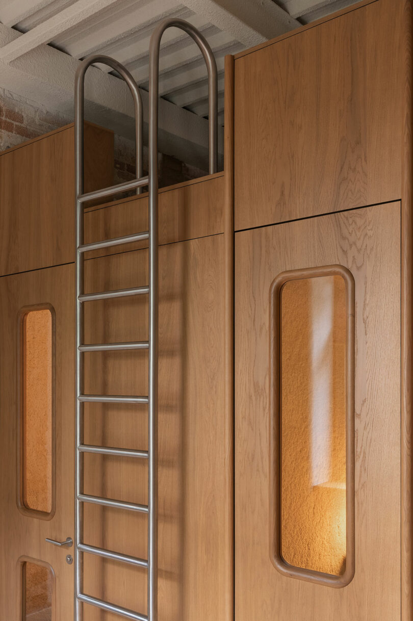 A metal ladder is attached to wooden built-in cabinets with rectangular windows, leading to an upper loft area.