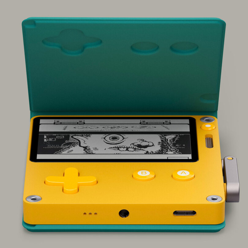 A yellow and green handheld gaming device with a crank, screen displaying a retro game, and visible control buttons on a gray background.
