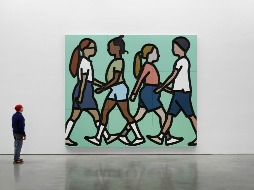 A person stands in front of a large wall art depicting four stylized figures walking, outlined in black, against a green background.