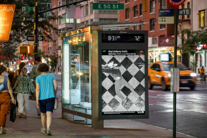 People walk past a bus stop in a city at dusk; an electronic display shows the 2025 Unframed black and white poster with a checkered pattern and digital clock reading 8:31 PM, temperature 72°F.