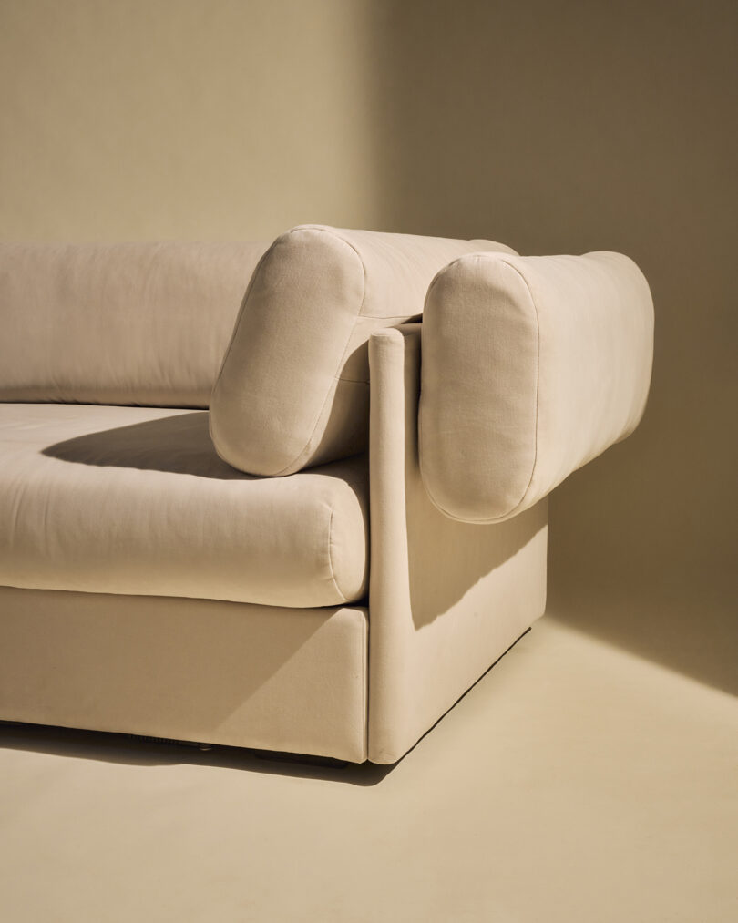 A close-up of a modern beige sofa with a unique geometric design and rounded, oversized armrests, set against a neutral background.