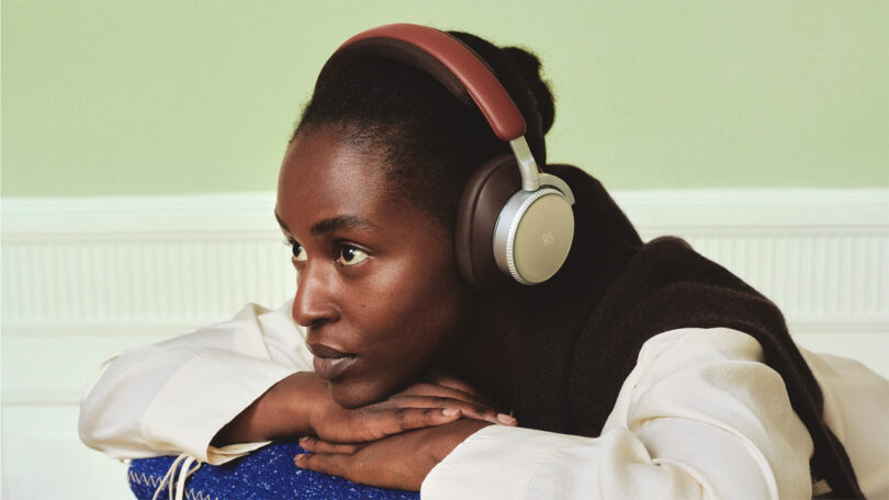 A person wearing over-ear headphones rests their chin on folded hands, looking to the side in a softly lit indoor setting.