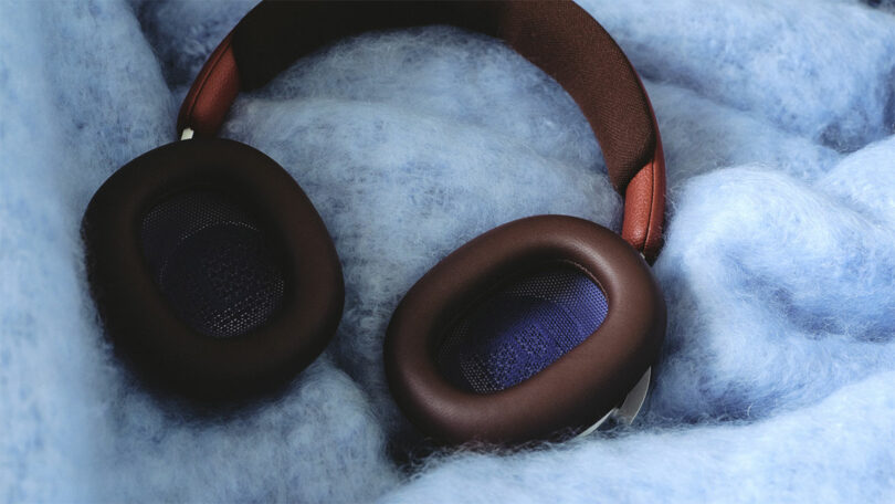 A pair of over-ear headphones with brown ear pads and headband resting on a soft, fluffy light blue surface.