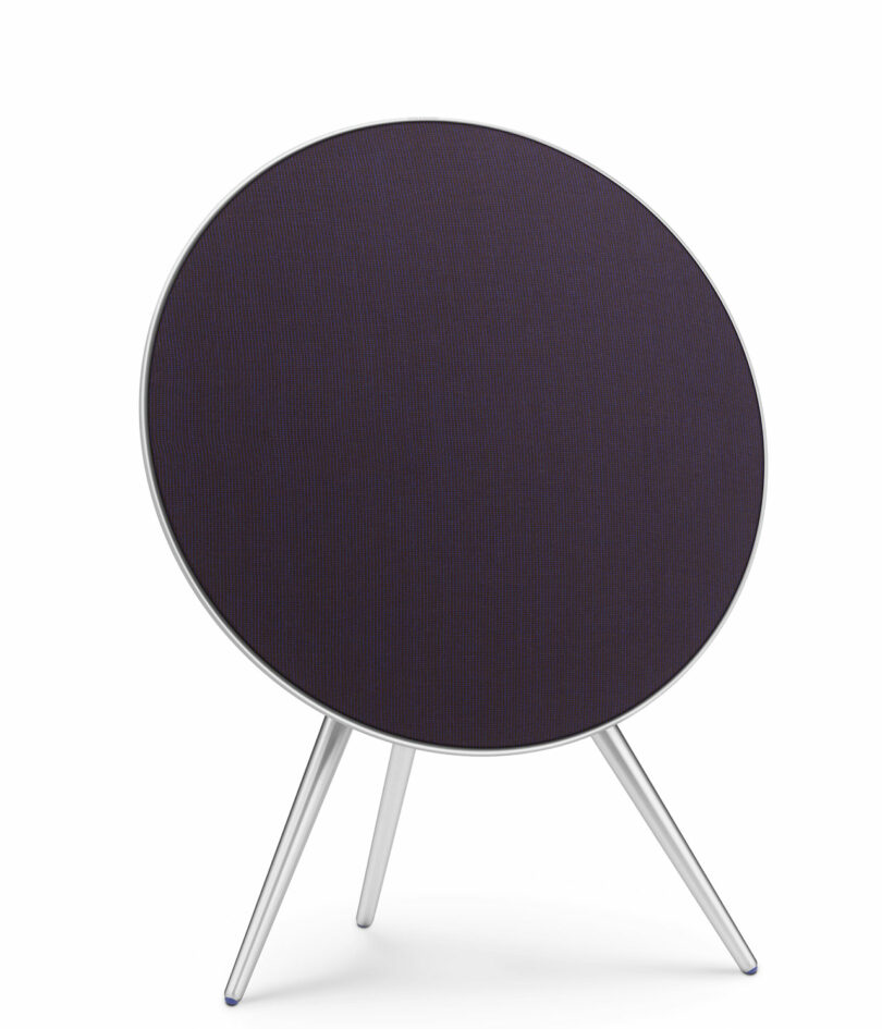 A round, dark-colored speaker with a slim metallic frame stands on three angled legs against a white background.