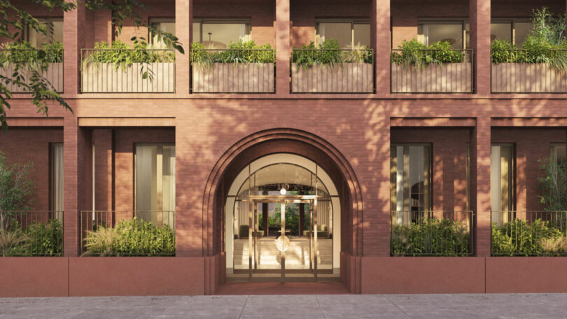 The image shows the brick facade of a Brent Buck building with a large arched entryway, balconies, and greenery along the windows and entrance.