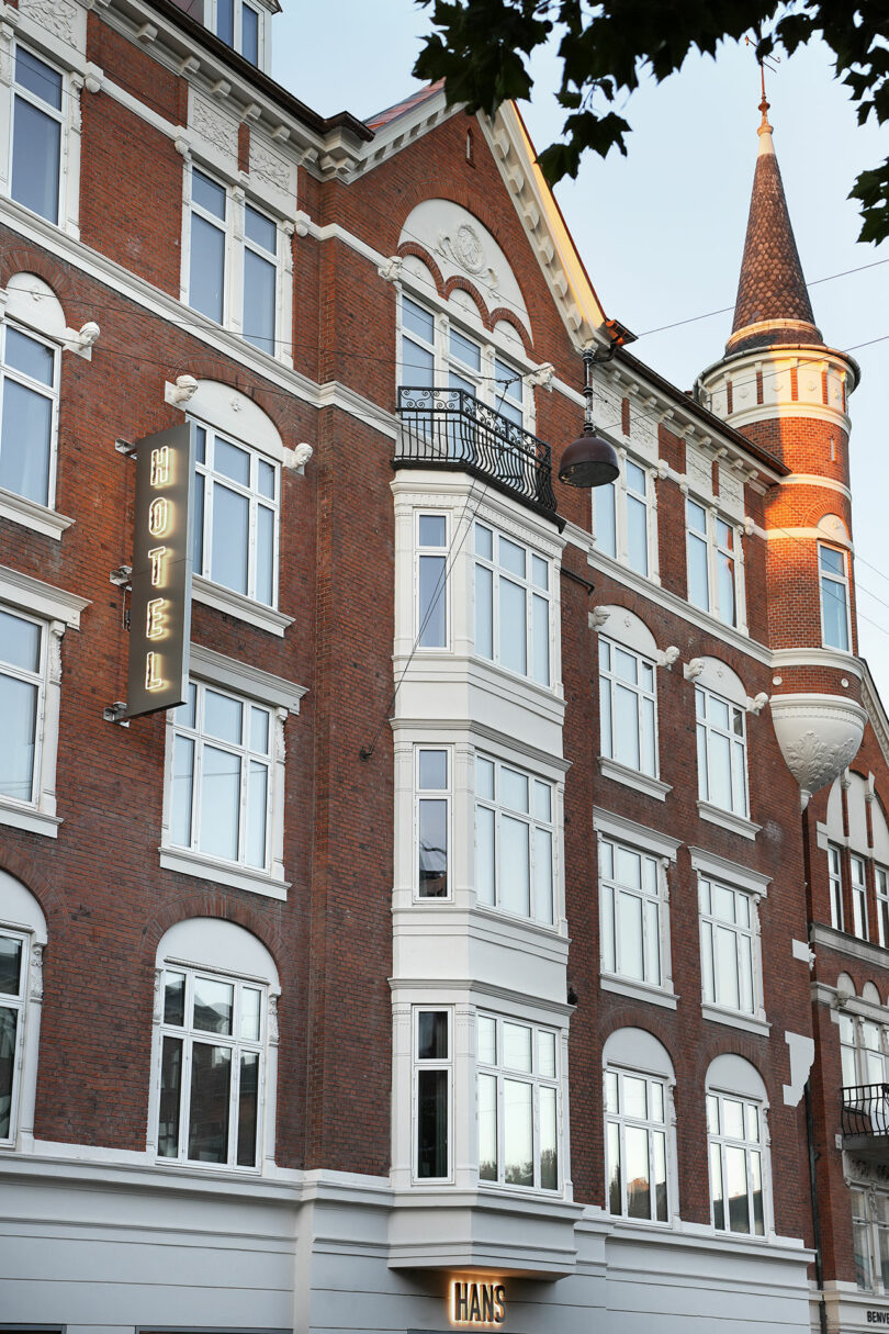A red-brick hotel building with white-framed windows, a decorative turret, a 