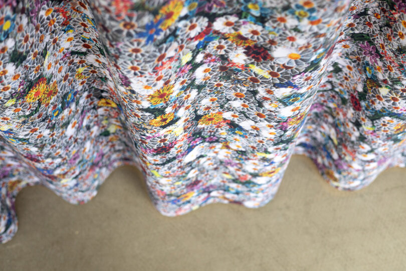 A close-up view of a fabric with a colorful floral pattern featuring daisies, draped in soft waves over a plain surface.