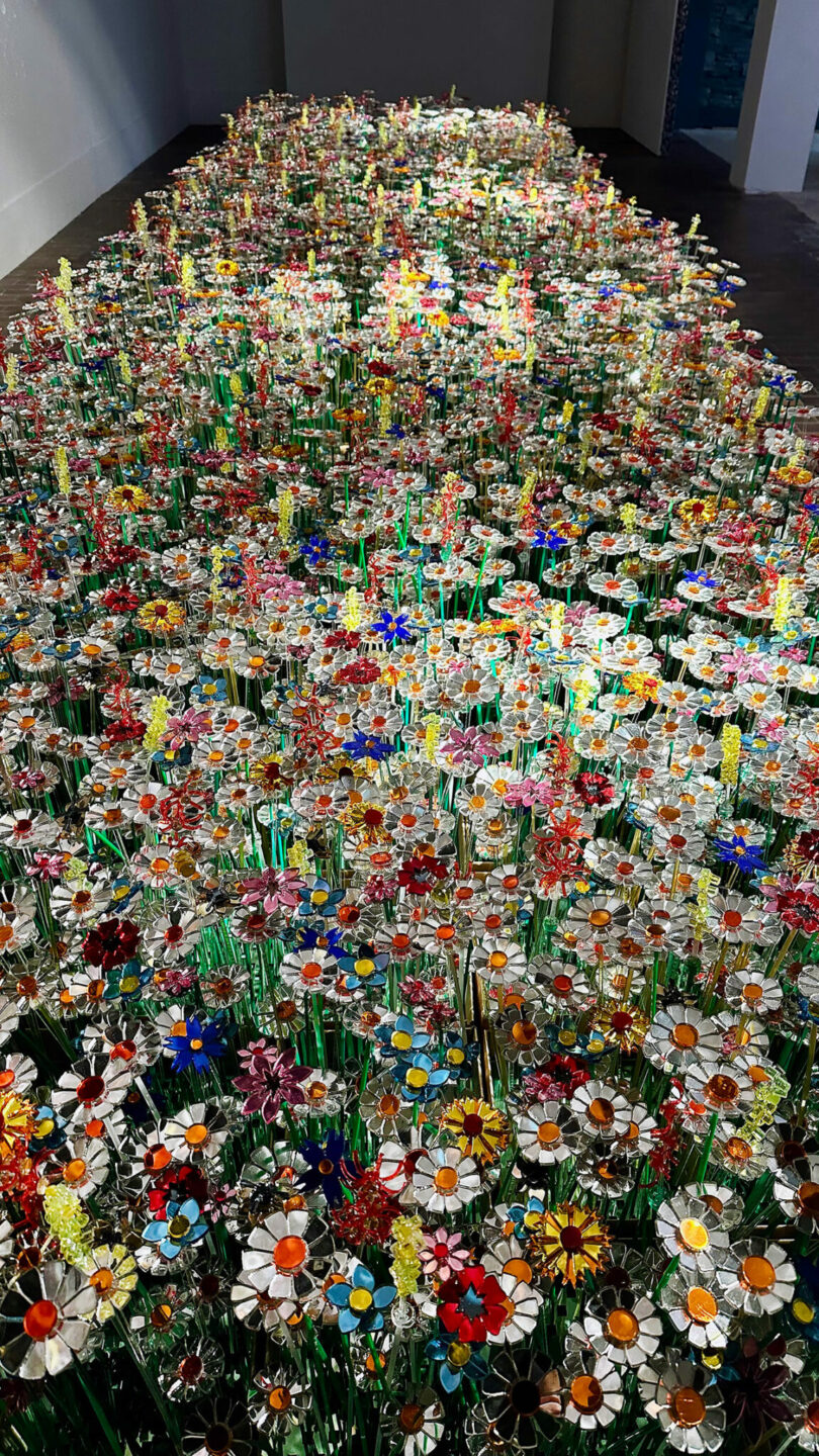 A large installation of colorful, artificial flowers made from various materials is arranged densely on the gallery floor, reflecting Diversiveness in its vibrant display—true to Mo Man Tai’s creative spirit.