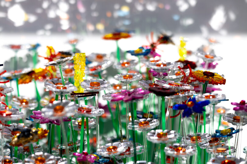 A close-up of colorful, flower-shaped sculptures made from translucent and shiny plastic pieces, set against a blurred background.