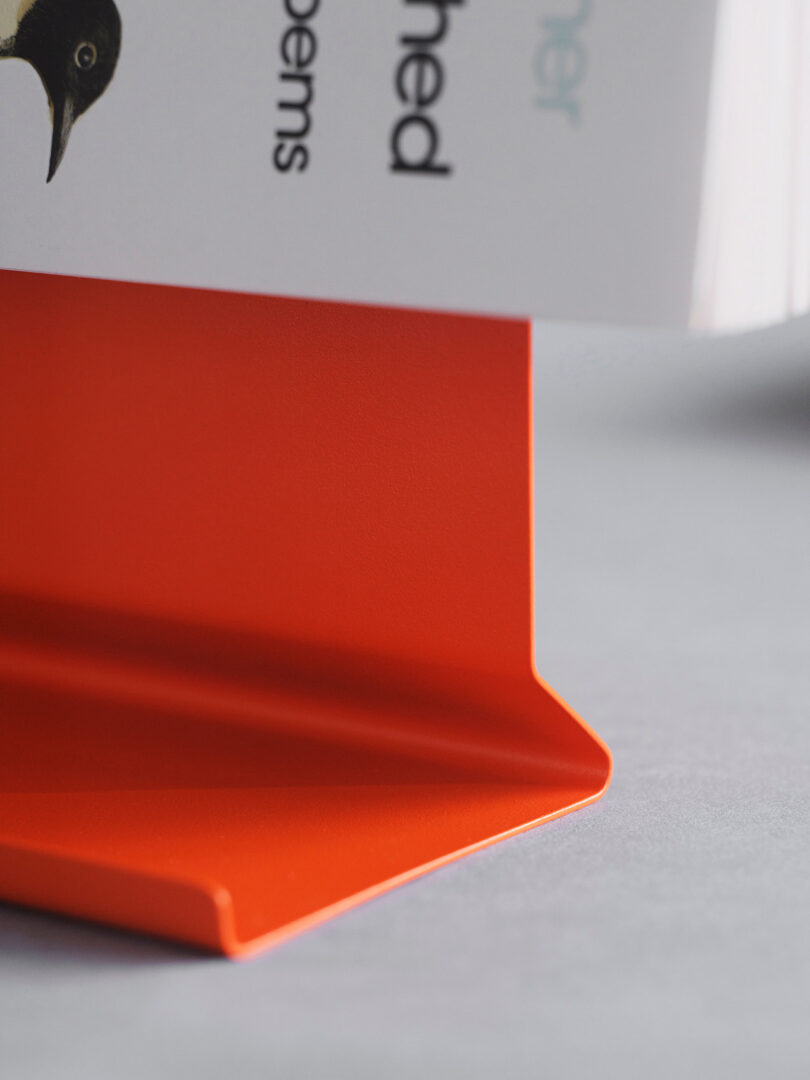 Close-up of a book resting on a bright orange metal bookend, with part of the book's cover and some text visible.