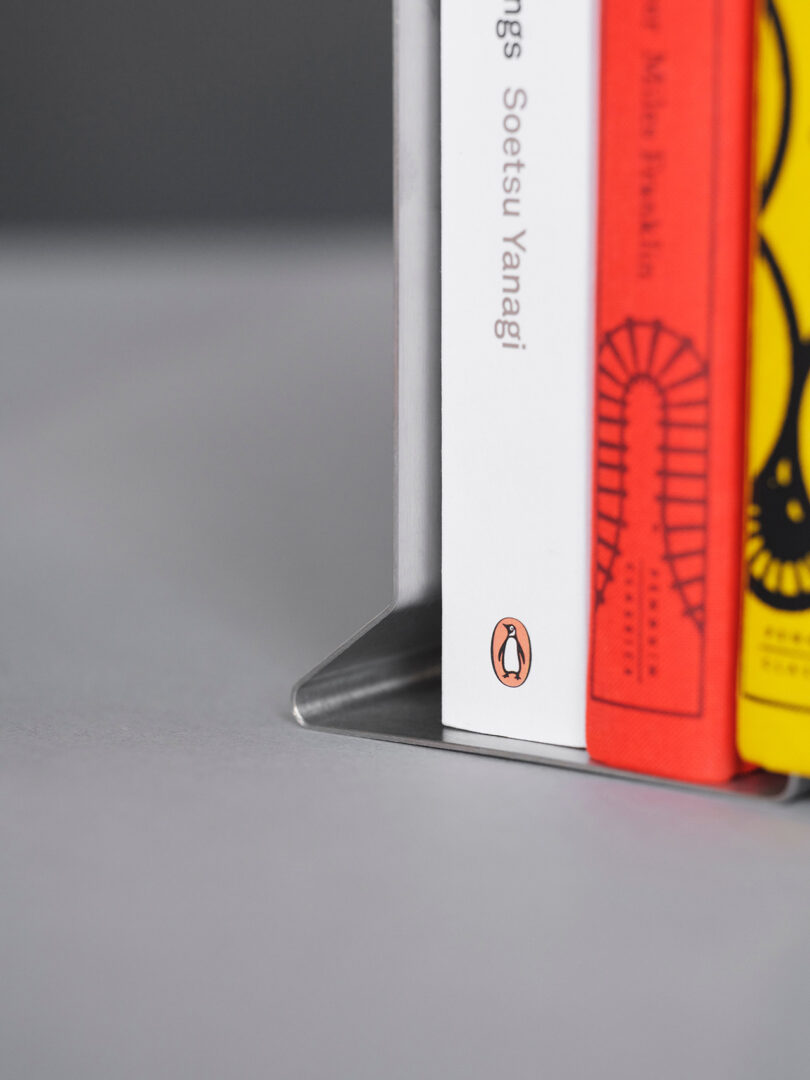 Close-up of a metal bookend supporting three vertically standing books, including a white book with the Penguin Books logo on its spine.