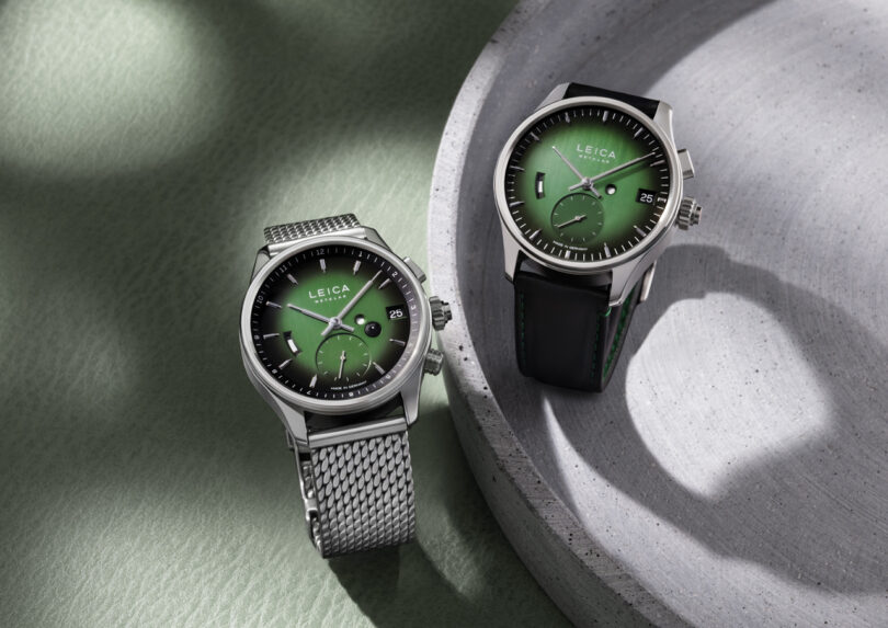 Two Leica watches with green dials are displayed side by side, one with a metal mesh strap and the other with a black leather strap, placed on a light green and gray background.