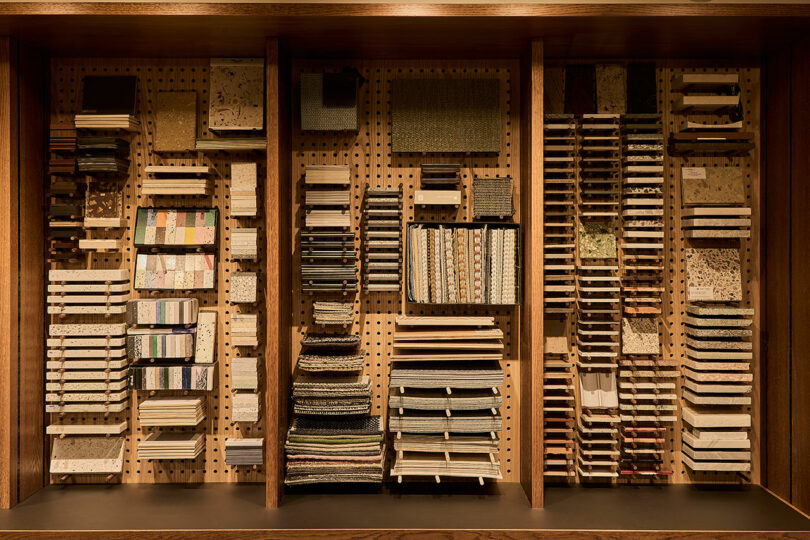 Shelves display neatly organized stacks of various material samples, including tiles and fabrics, against a wooden pegboard wall.