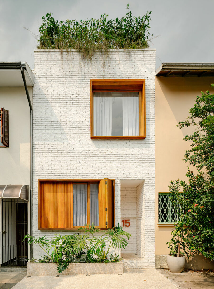 A modern white brick townhouse with large wooden-framed windows, a rooftop garden, and the number 15 by the entrance.