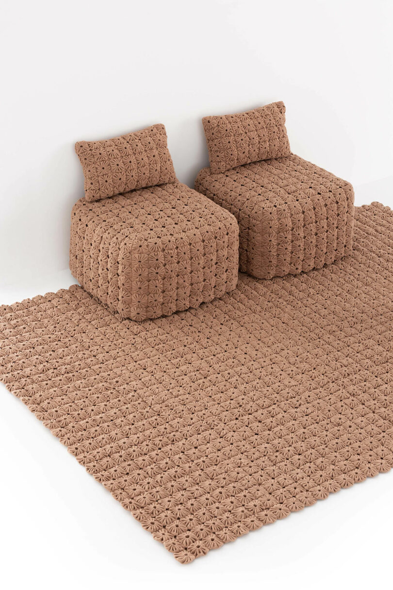 Two brown, textured, woven chairs with matching cushions sit on a large, matching woven rug against a white wall.