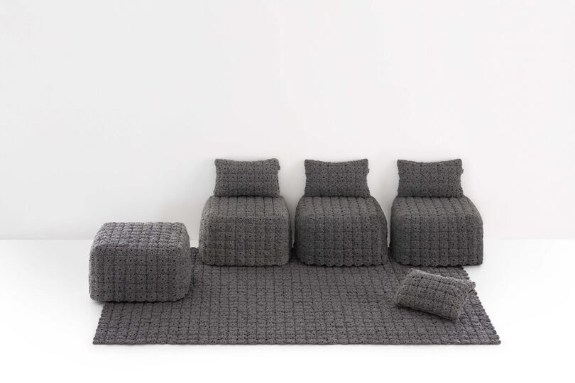 A set of gray, crochet-textured modular furniture including three chairs, a pouf, a square ottoman, and a matching rug, all arranged against a white background.