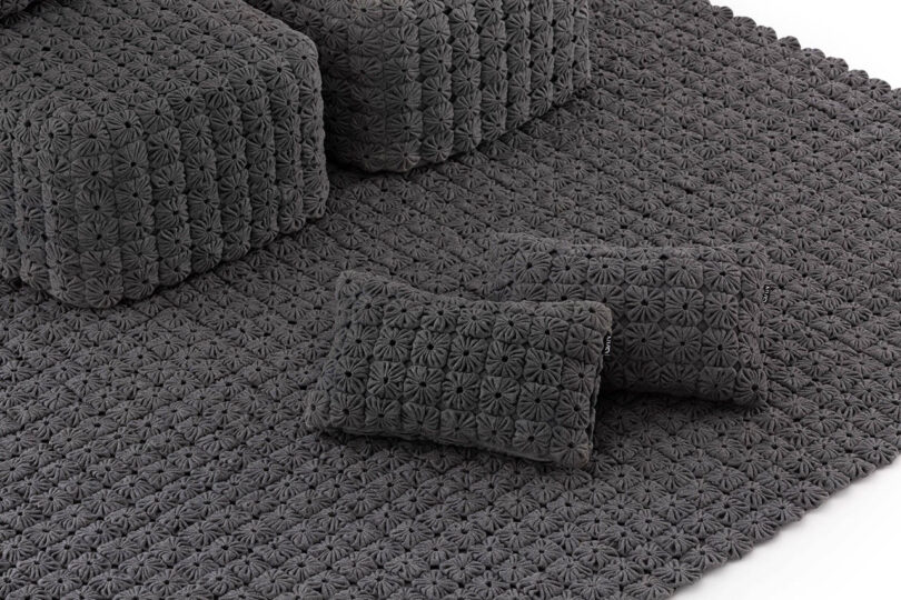 Two rectangular, textured dark gray cushions rest on a matching patterned rug beside similarly textured seating furniture.