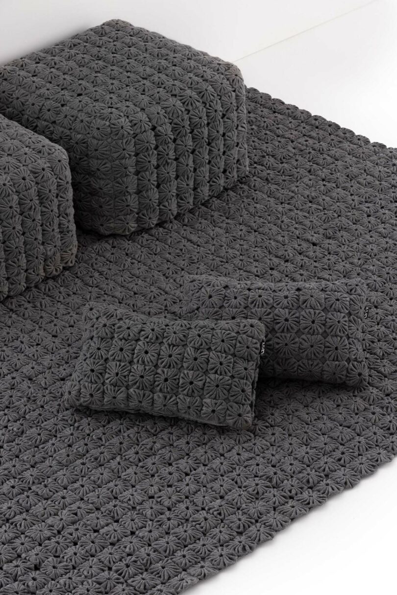 Two rectangular pillows and two square cushions rest on a textured dark gray mat, all featuring the same geometric, flower-like pattern.