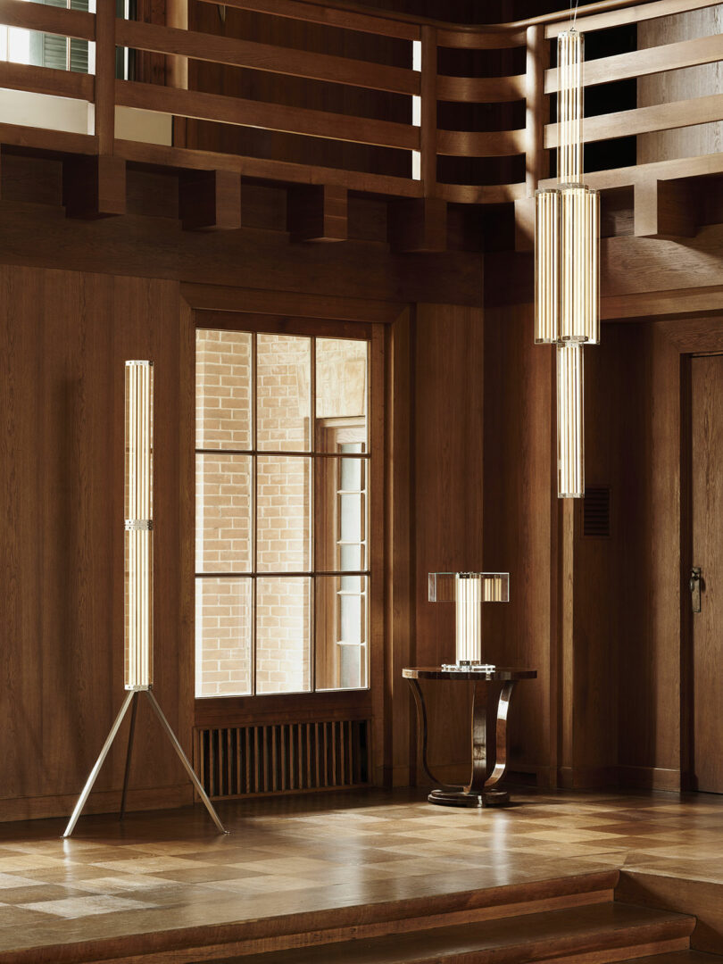 A wood-paneled room with a large window, displaying modern vertical light fixtures on a tripod stand, ceiling, and a table.