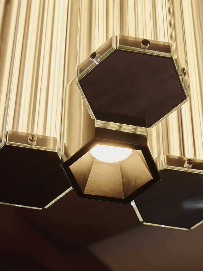 Close-up of a modern hexagonal pendant light with brass and glass elements, showing one illuminated bulb.