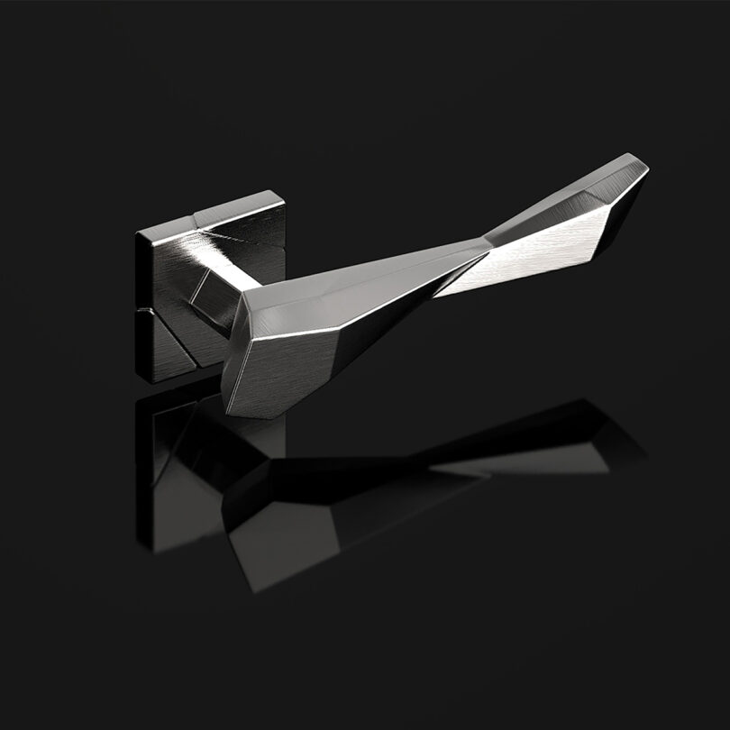 A modern, angular metallic door handle is mounted on a rectangular backplate against a black background, reflecting light and its own image on the surface below.