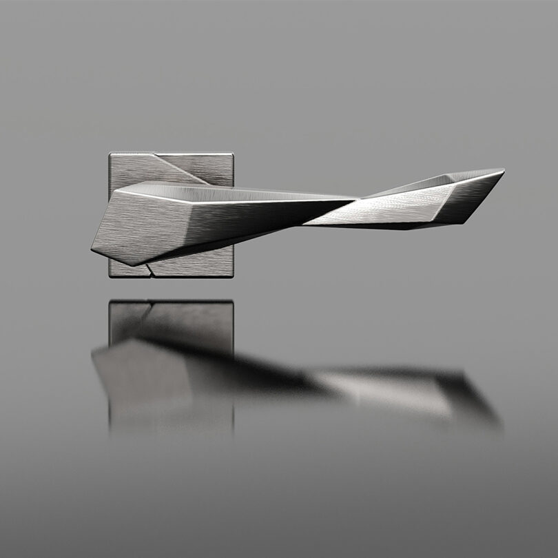 A modern, angular metallic door handle with a brushed finish is mounted on a rectangular backplate against a gray background.