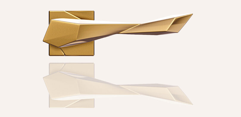 Geometric gold door handle with angular design, mounted on a square backplate, reflected on a glossy surface.