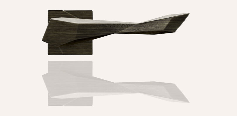 A modern, geometric wooden door handle with an angular design is mounted on a square backplate, casting a faint reflection below.