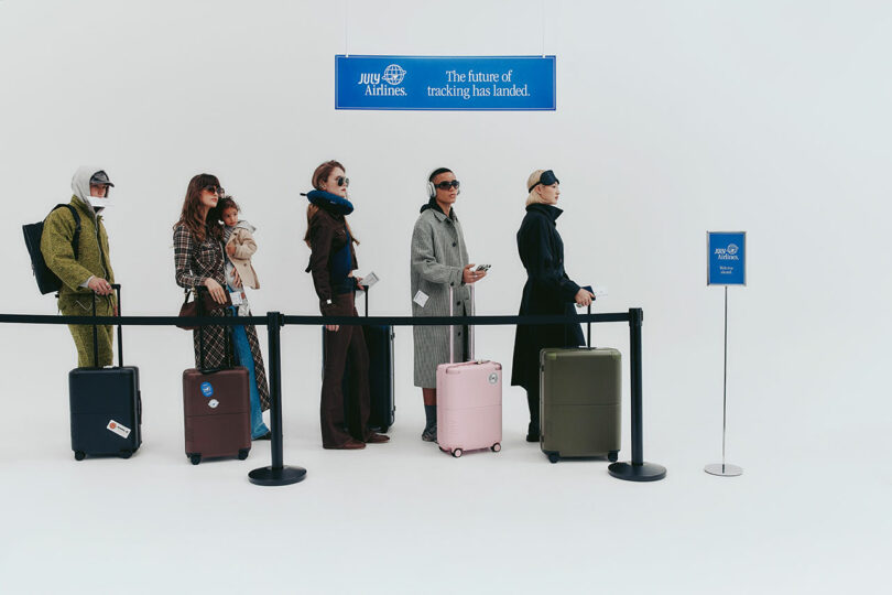 Six people with suitcases stand in line at an airline check-in counter with a blue sign reading 
