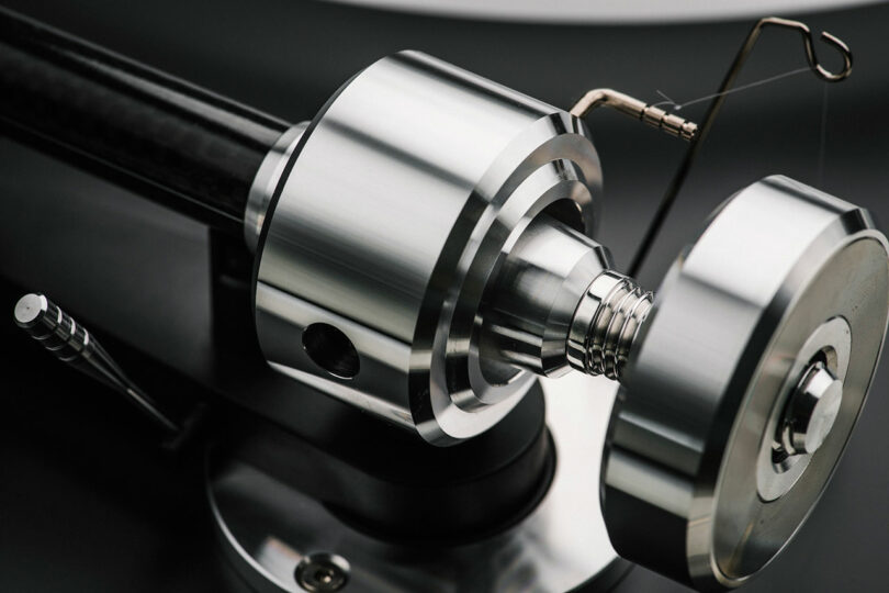 Close-up of a polished metal tonearm mechanism on a turntable, showing intricate details and precise engineering components.