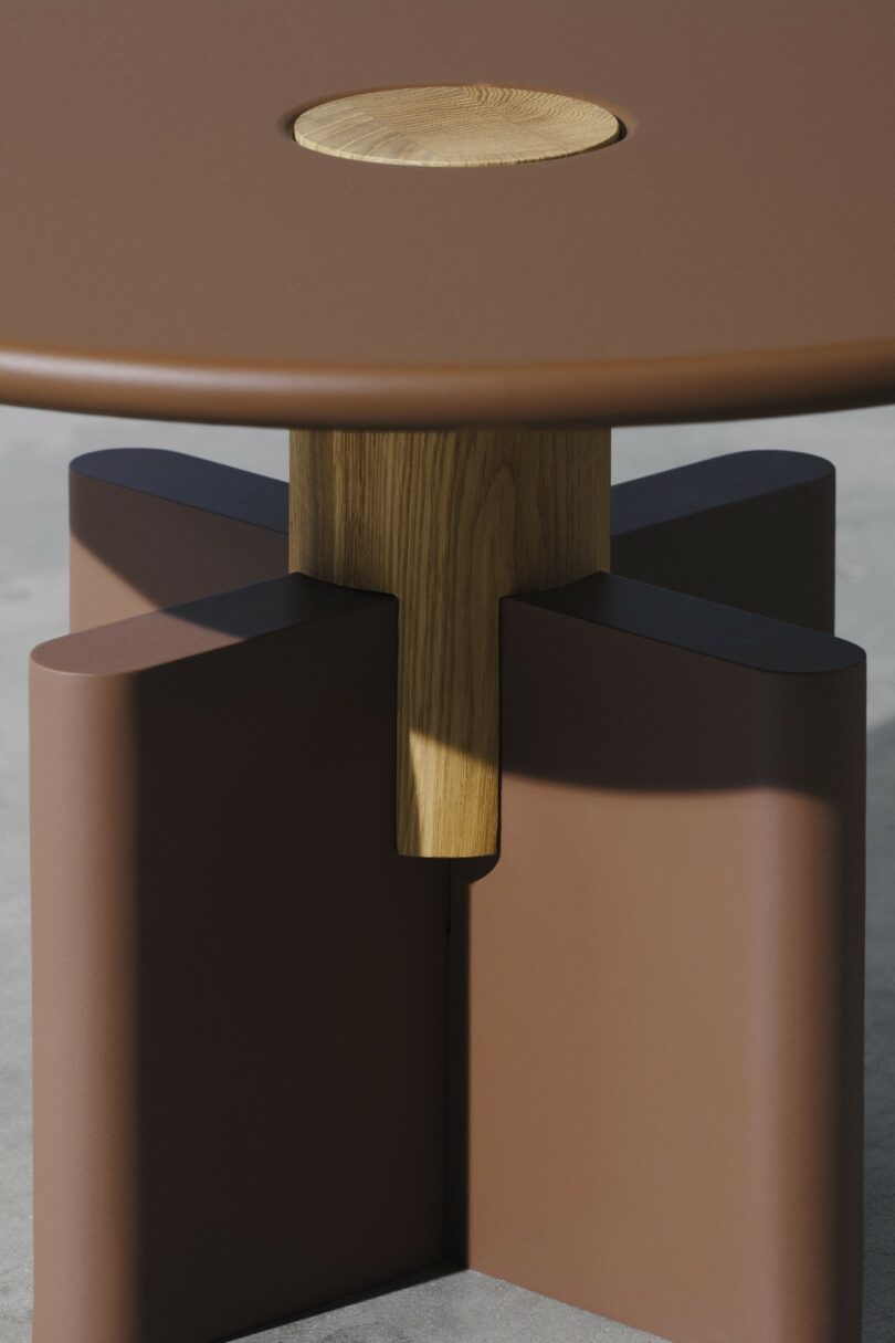 A round brown table with a wooden circular inlay on top and a geometric wooden and brown base, positioned on a smooth concrete floor