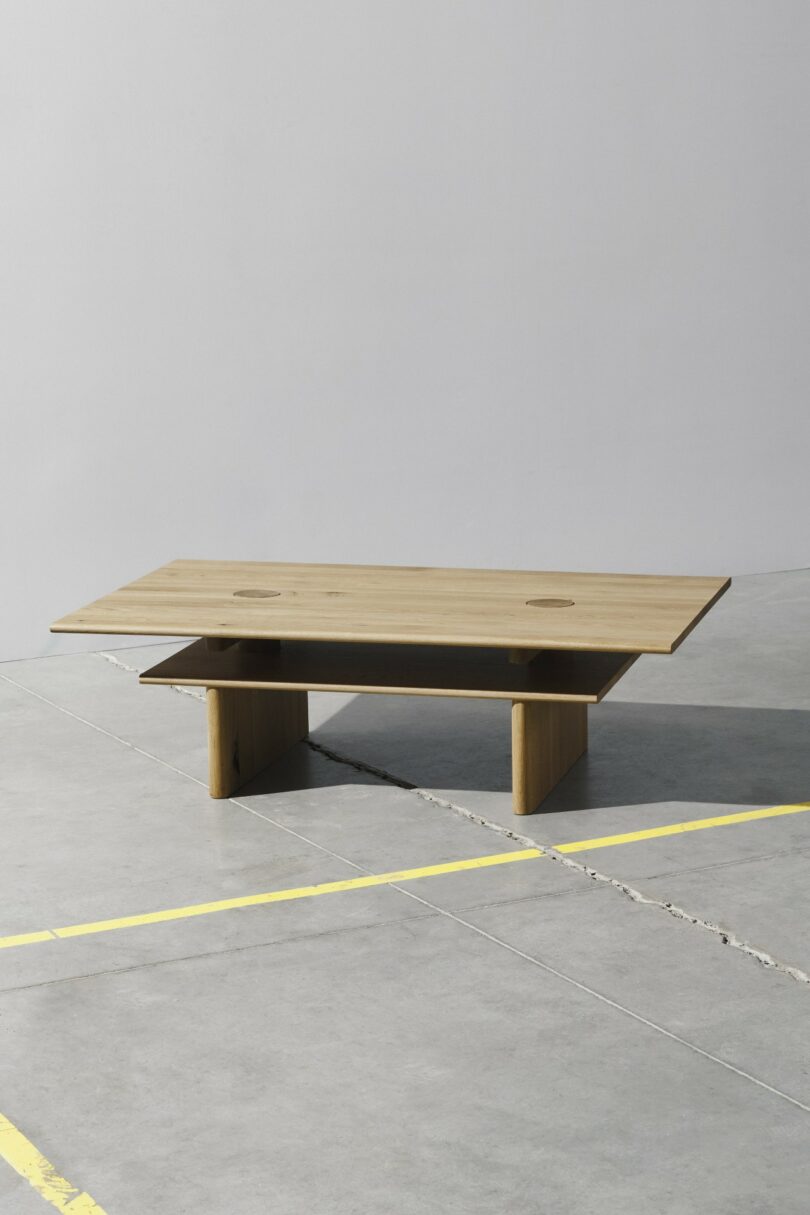 A rectangular wooden coffee table with a flat top and a lower shelf, positioned on a gray concrete floor with yellow parking lines