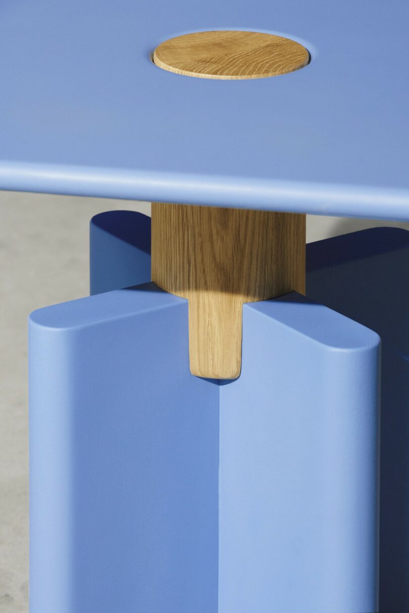 A close-up of a blue table with a circular wooden inlay and a wooden support connecting the legs, featuring modern geometric design