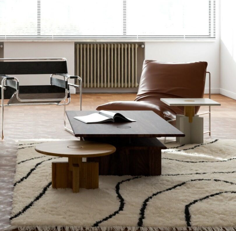 A modern living room with a leather lounge chair, a black-and-white armchair, a low coffee table, a side table, and a rug with black wavy lines. An open book rests on the table.