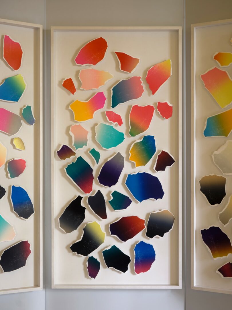 Three white folding panels display colorful abstract shapes in a bright room with classical wall art and marble flooring