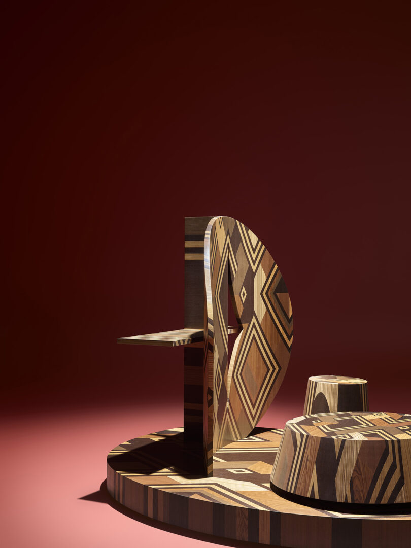 Geometric wooden furniture pieces with inlaid patterns set against a deep red background and floor.