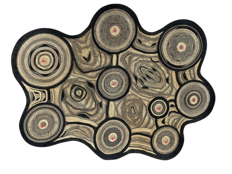 An abstract, irregularly shaped textile-lamp with concentric circular patterns in black, beige, and red tones on a white background