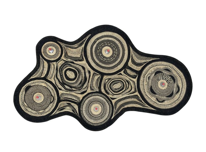 An abstract, irregularly shaped textile-lamp with concentric circular patterns in black, beige, and red tones on a white background