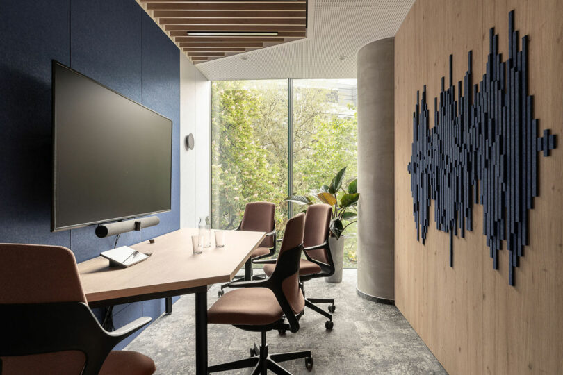 A modern BIT CREATIVE conference room with a large wall-mounted screen, four brown office chairs around a rectangular table, floor-to-ceiling window, and abstract wall art.