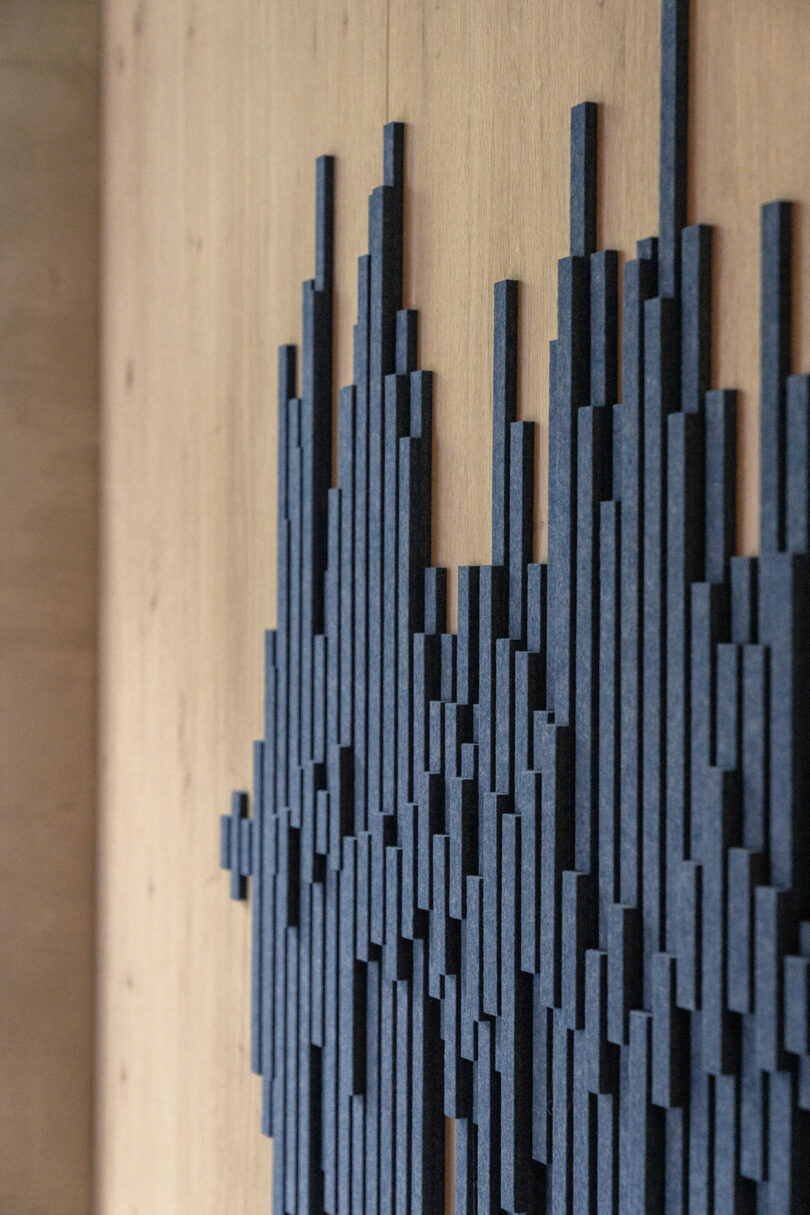 Vertical black rectangular foam panels are arranged in varying heights on a light wood wall, forming an abstract geometric pattern—a signature touch from BIT CREATIVE.