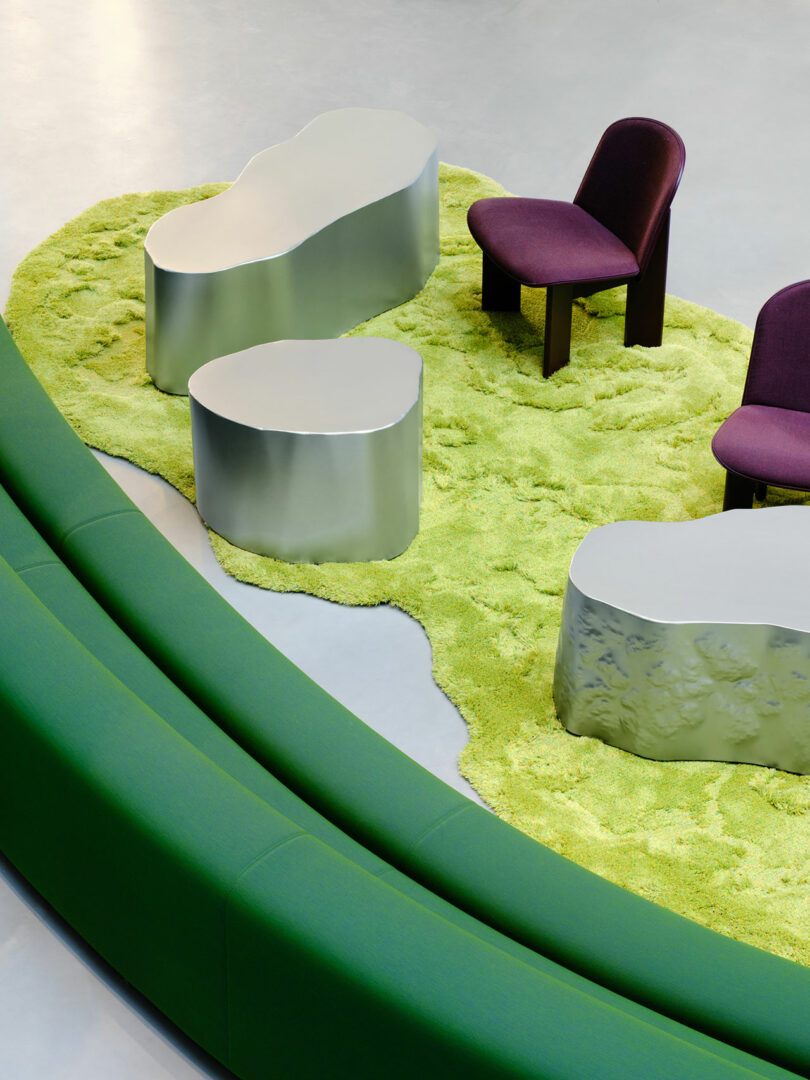 A curved green bench surrounds three metallic tables and two purple chairs on a textured, irregularly shaped green rug.