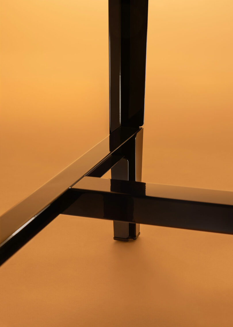 Close-up view of the black metal legs and cross-support of a table or chair against a warm, orange background.
