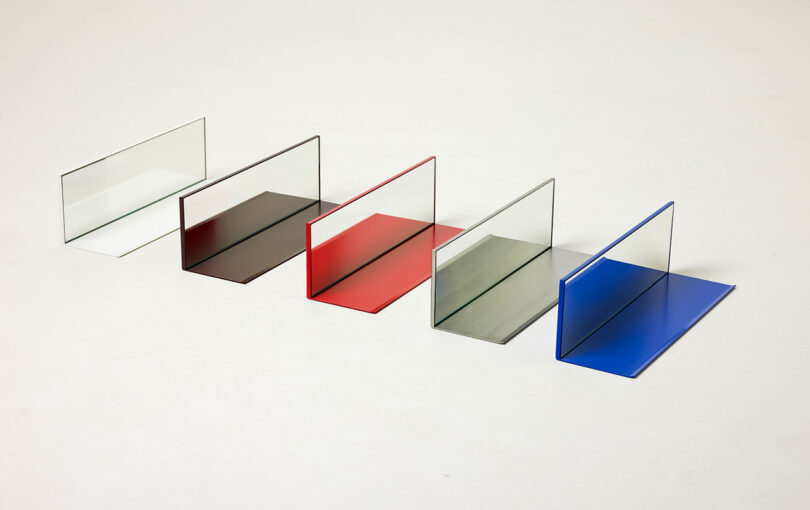 Five rectangular glass sheets with colored bases—white, brown, red, gray, and blue—arranged in a row on a plain light background.