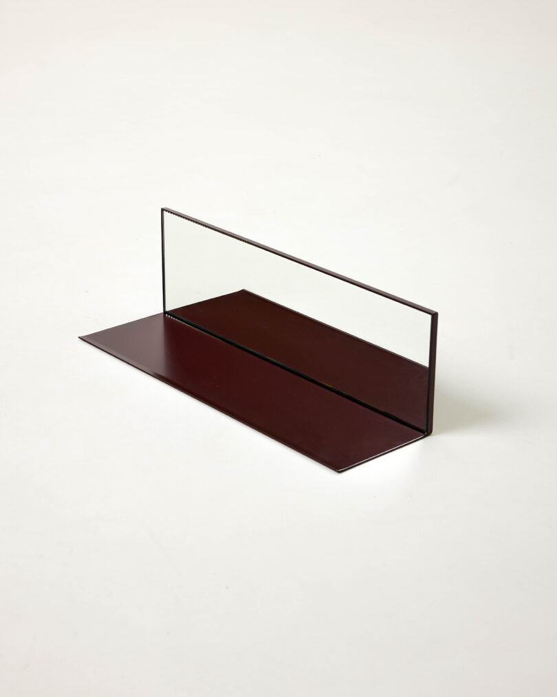 A rectangular glass pane is vertically mounted on a flat, dark red rectangular base, set against a plain white background.