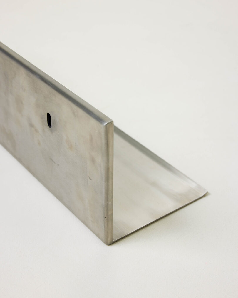 A metal L-shaped bracket with a small oval hole near the top, placed on a light, neutral surface.