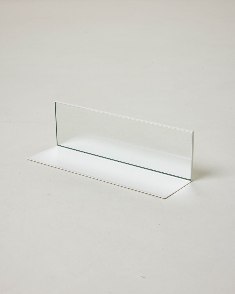 A rectangular glass pane stands vertically on a flat white surface, casting a faint reflection and shadow.