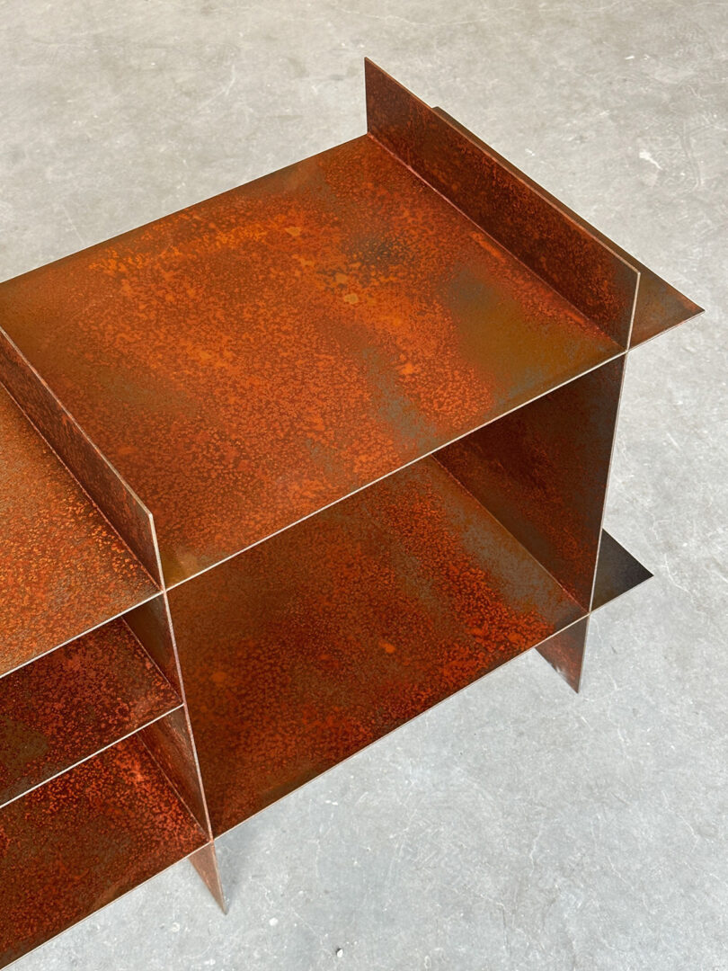 Rectangular metal shelf unit with a rusted, weathered finish, positioned on a concrete floor.