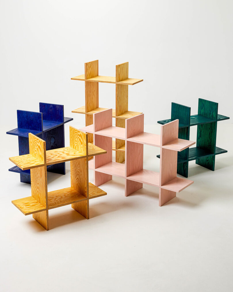 Four colorful, modular wooden shelving units in yellow, blue, pink, and green are arranged on a plain white background.
