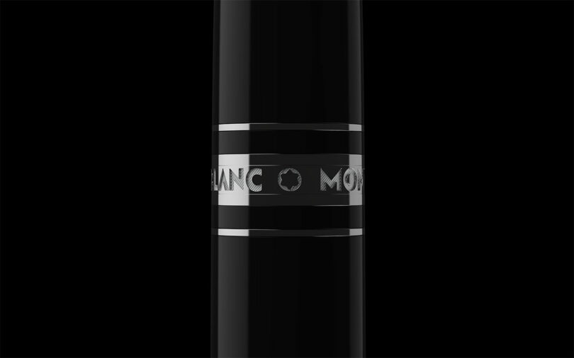 Close-up of a black pen barrel with silver metal bands, featuring partially visible engraved text reading 